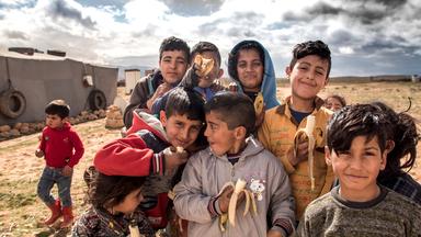 Kriegsfotografie - Kinder eines Flüchtlingscamps im Libanon. Die Kinder essen alle eine Banane und lächeln in die Kamera.