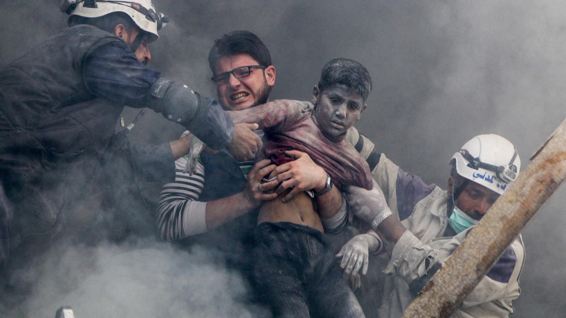 Kriegsfotografie - Szene von einem Bombenangriff in Aleppo. Ein Mann mit einem Jungen im Arm werden gerettet.