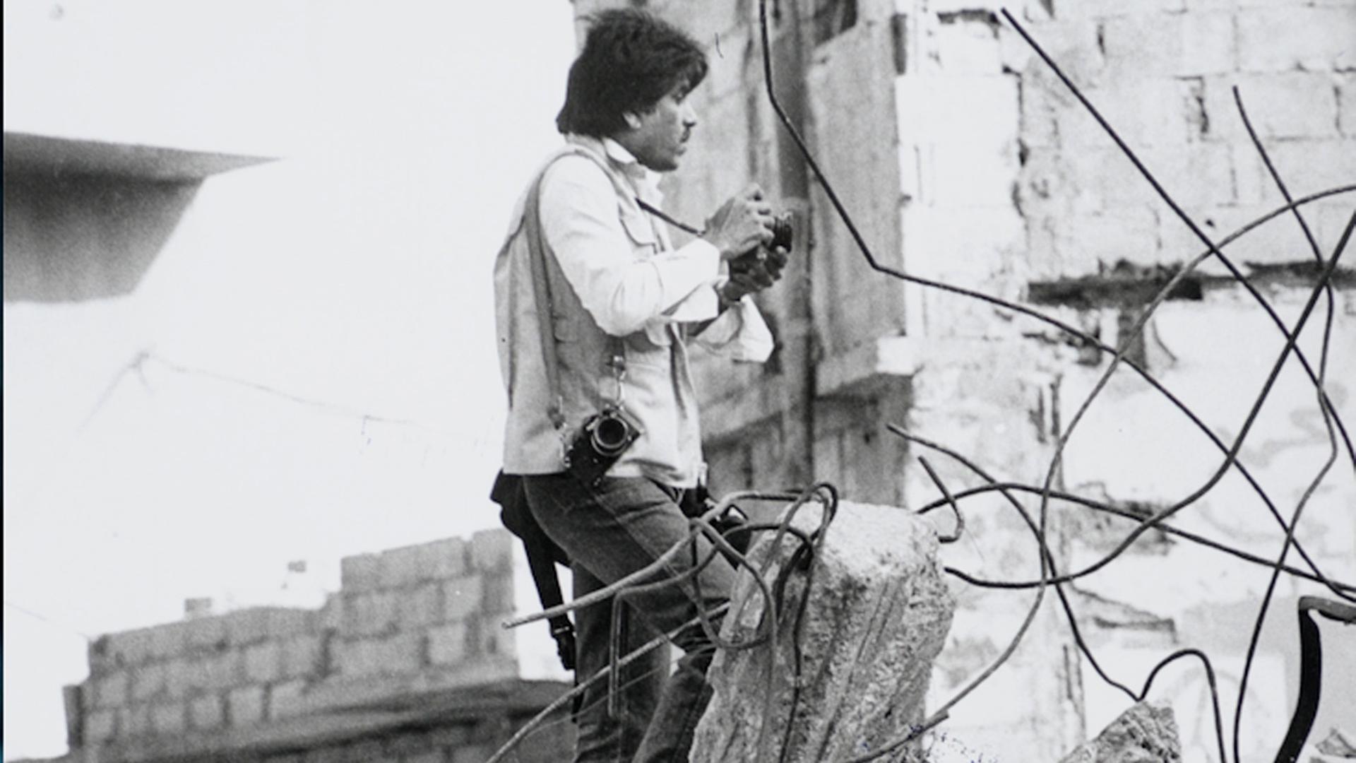 Kriegsfotografie - Fotograf steht auf einem Schuttberg und hält eine Kamera in der Hand.