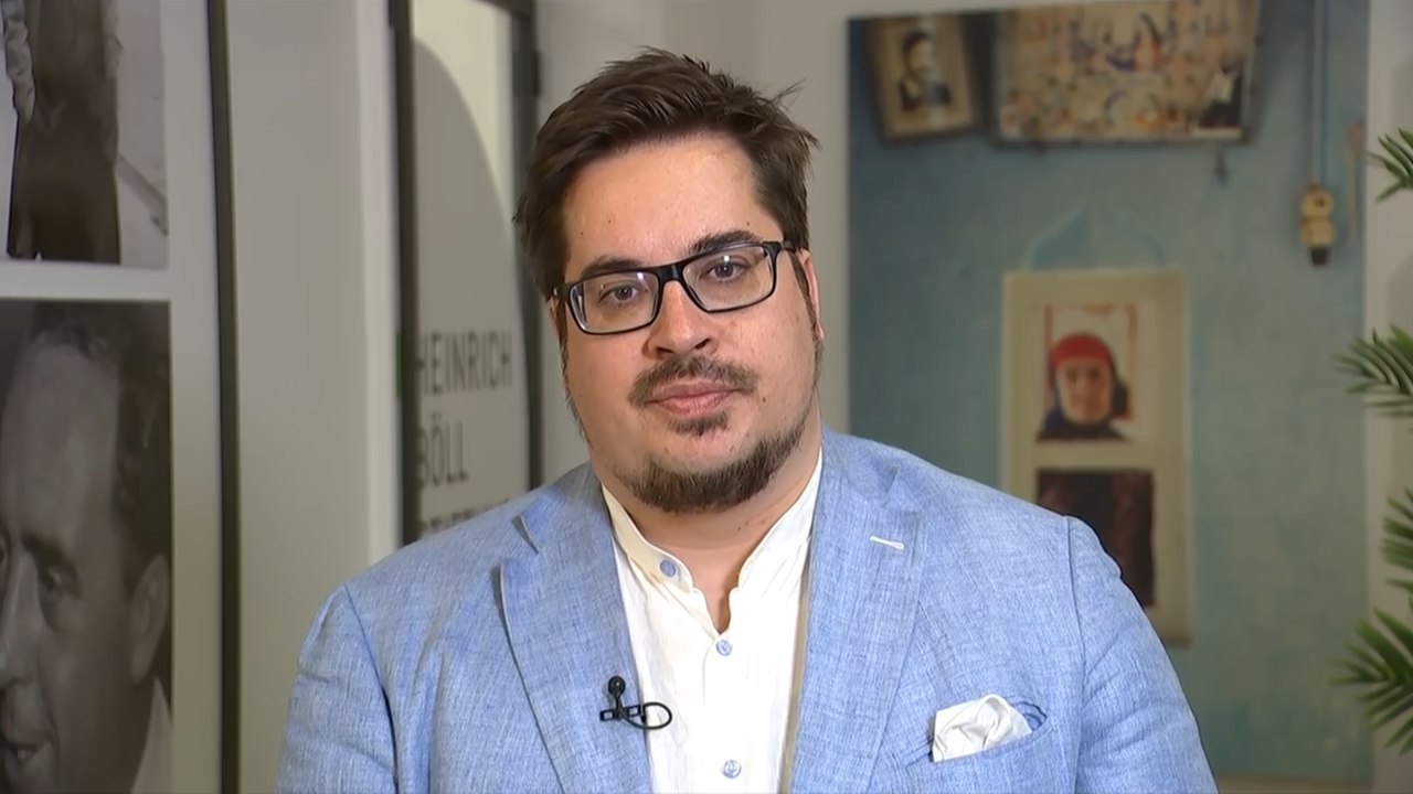 Ein junger Mann mit Bart, Brille und hellblauem Anzug.