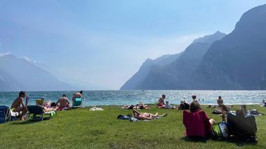 Eine mit Menschen gefüllte Liegewiese an einem See.