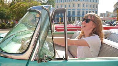 Eine Frau in einem türkisfarbenen Oldtimer-Cabrio.