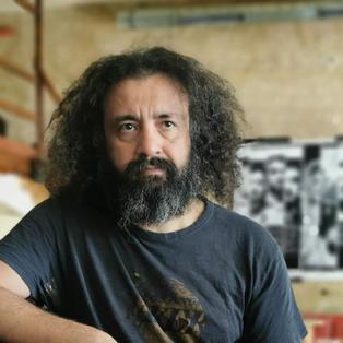 "Kültür für Deutschland“: Fotograf Sedat Mehder in seiner Bar in Berlin. Er hat einen Arm auf den Tresen gestützt. Im Hintergrund sieht Sessel und Sofa, an der Wand hängt eine Fotografie.