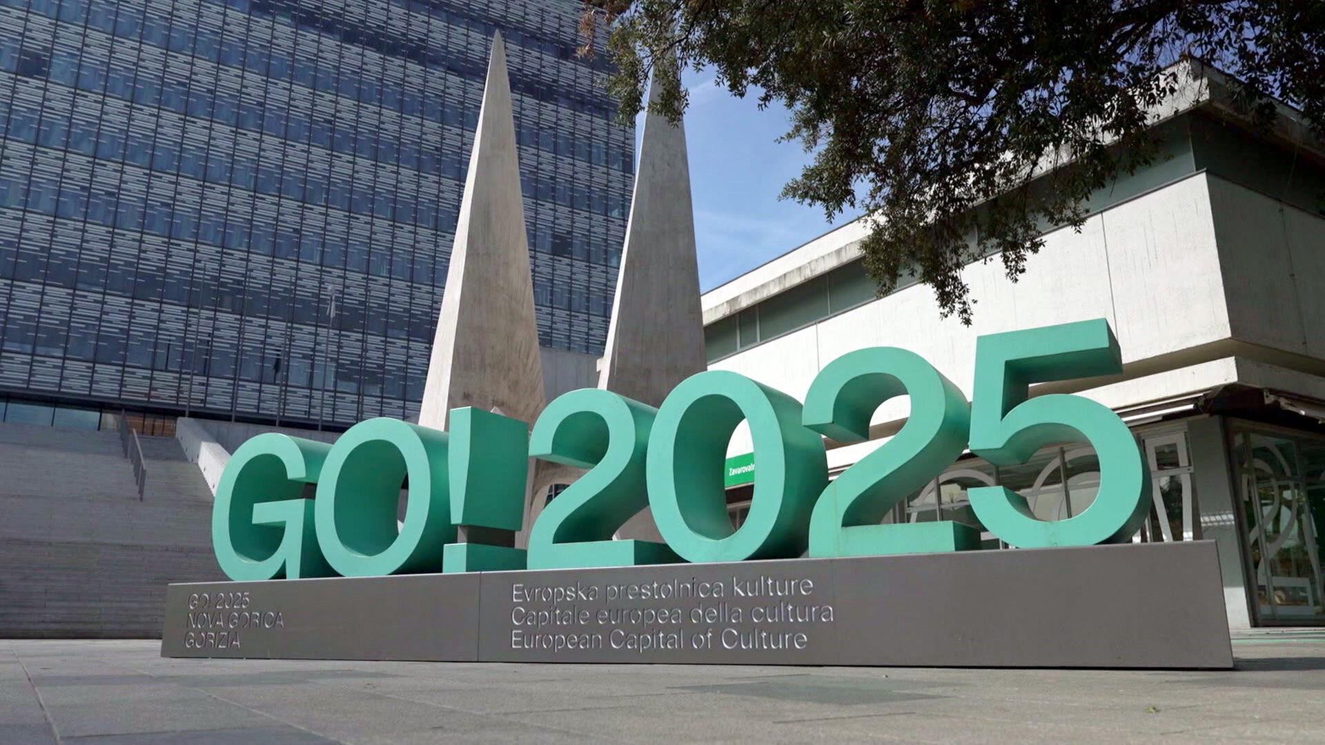 Großes türkisfarbenes Schriftzeichen GO! 2025 vor moderner Architektur in Nova Gorica, Symbol der europäischen Kulturhauptstadt 2025