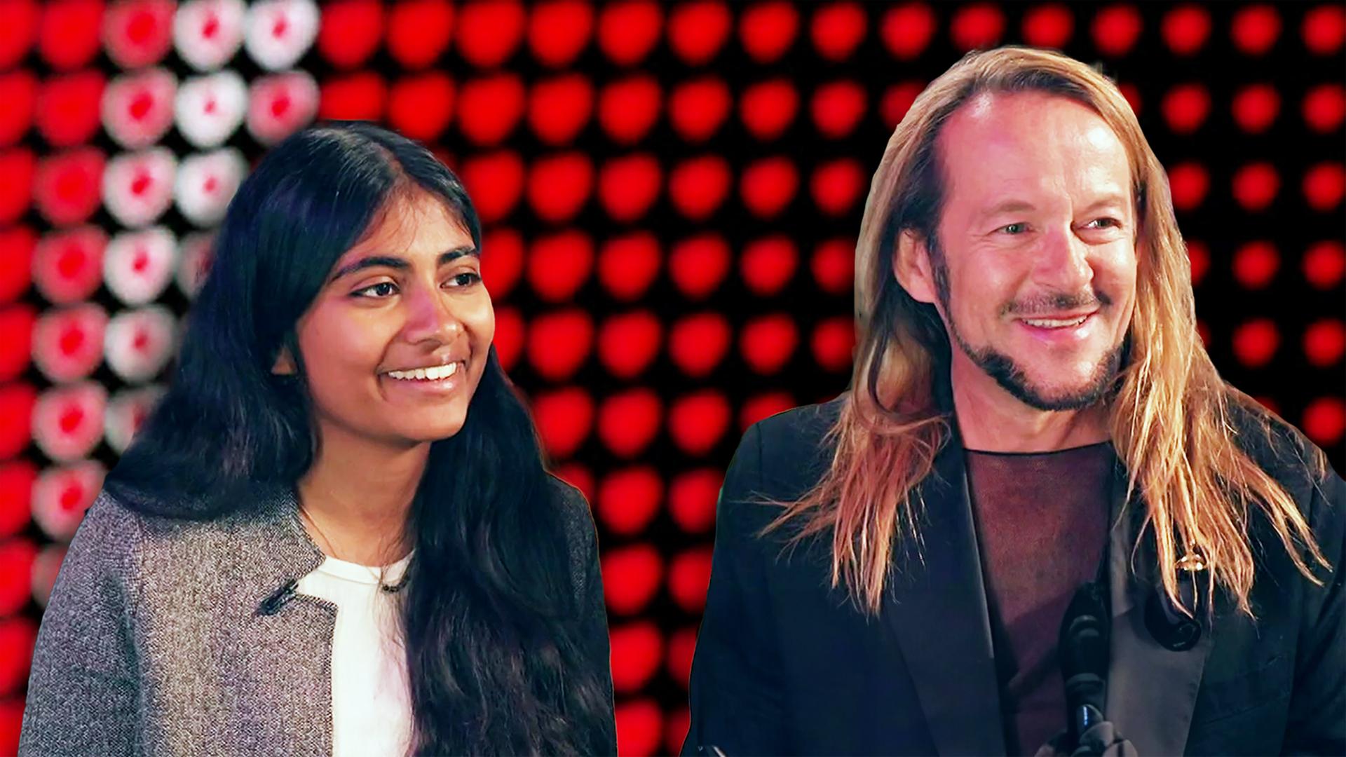 Zwei Personen in fröhlicher Gesprächssituation vor einer ESC-inspirierten Bühnenwand mit roten Lichtpunkten.