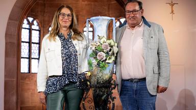 Eine Frau und ein Mann stehen zwischen einer großen Vase