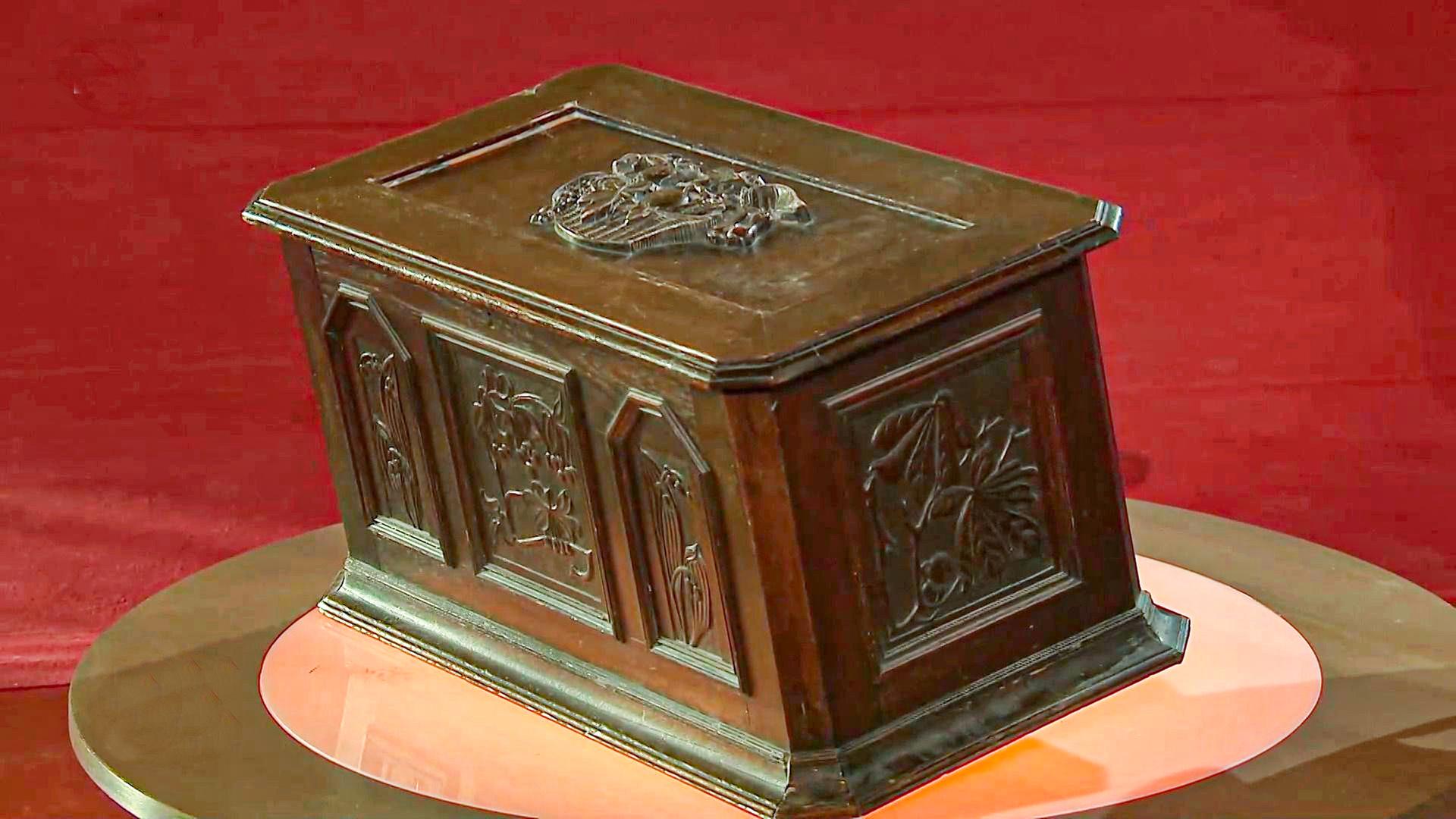 dunkle Holztruhe mit Schnitzereien in Form von Gebäuden im Deckel