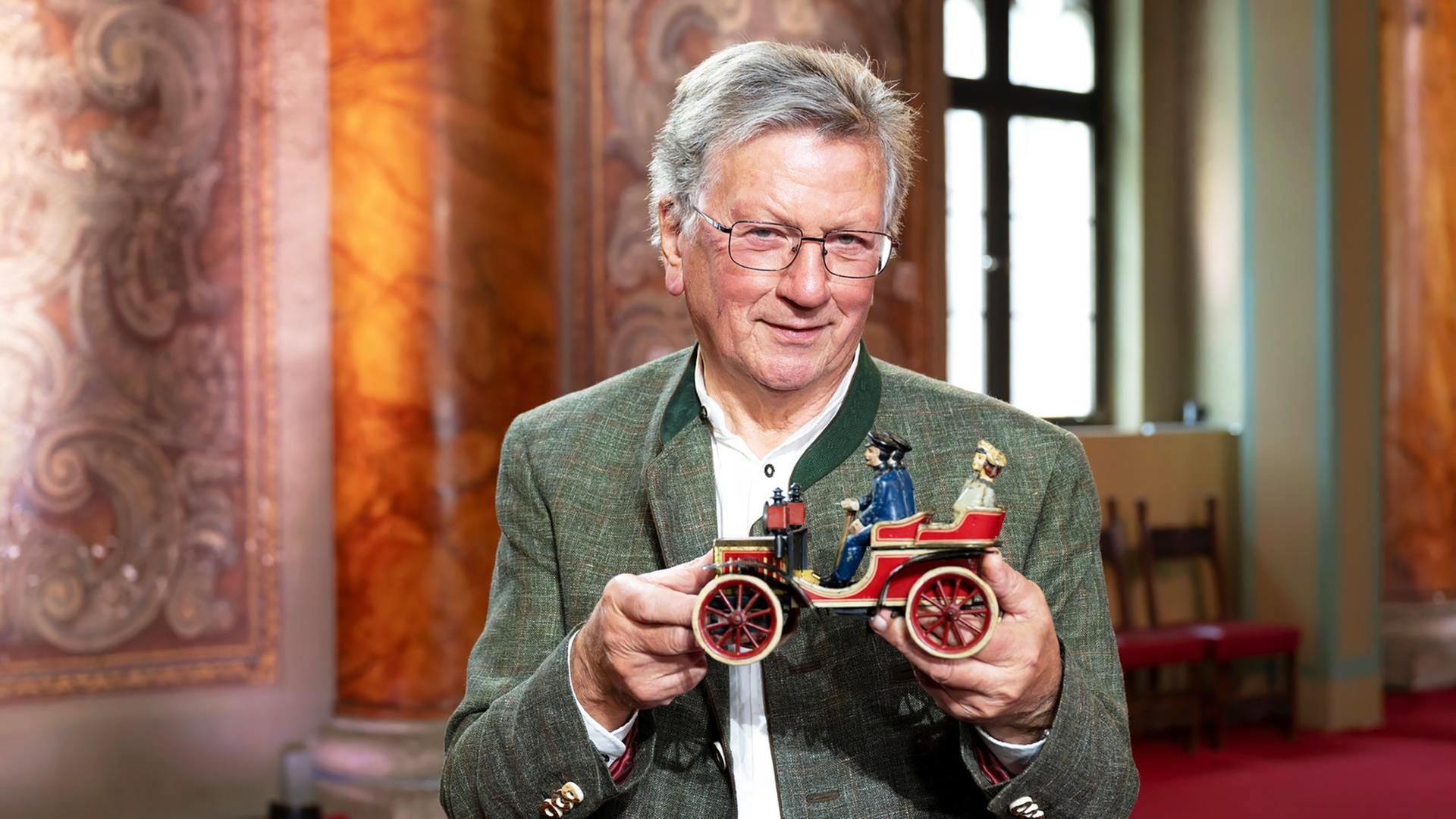 Ein Mann hält einen Tourenwagen von einer umfangreichen Spielzeugsammlung in den Händen.
