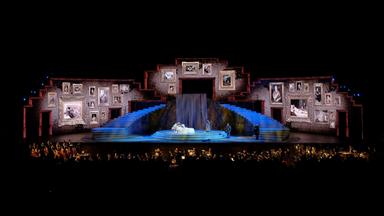 "Aus der Arena di Verona: Giuseppe Verdi - La Traviata": Eine riesige bunt ausgeleuchtete Bühne mit Orchester in der dunklen Arena.