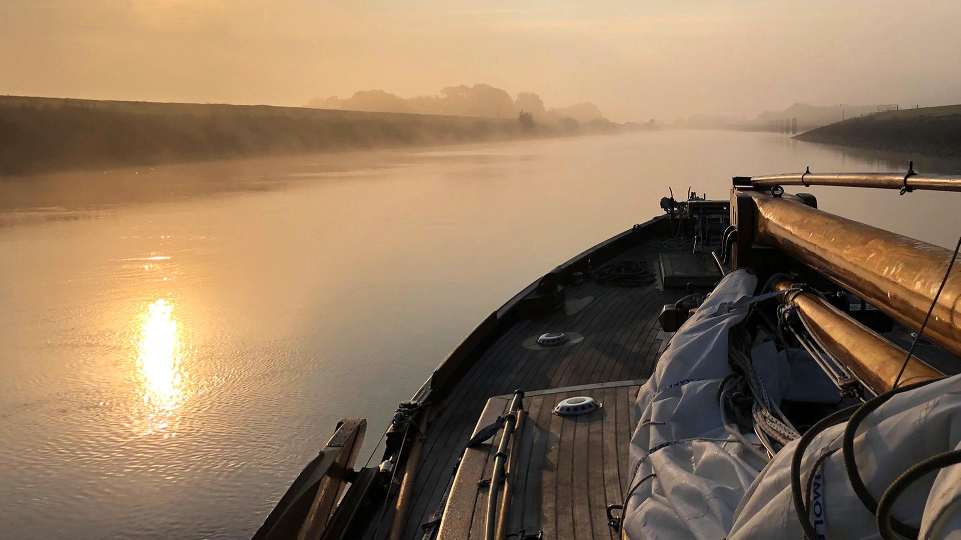 Ein Segelboot, das an einem nebligen Morgen einen Kanal entlanggleitet.