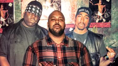 Drei Männer stehen zusammen, der Rapper Biggie Smalls, der Rapper Tupac Shakur und Suge Knight, Plattenboss, und zeigen den Mittelfinger.