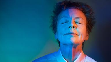 Eine Frau steht mit geschlossenen Augen und nach oben gewandtem Gesicht in buntem Licht.