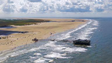 Pfahlbauten am breiten Sandstrand von St. Peter-Ording bei Ebbe, mit weiten Himmel und Nordsee im Hintergrund.
