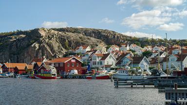Küstenort Fjällbacka mit bunten Häusern am Wasser, dominiert vom imposanten Vetteberg im Hintergrund.