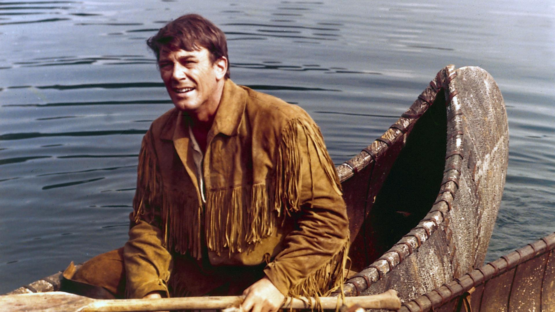 Lederstrumpf (Hellmut Lange) sitzt in einem Kanu auf dem Wasser