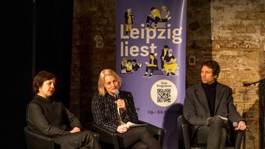 Zwei Frauen und ein Mann sitzen auf einer Bühne vor einem Aufsteller, auf dem Leipzig liest geschrieben steht.