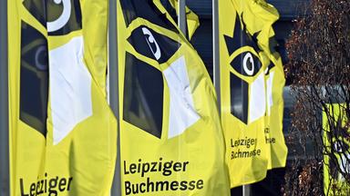 Gelbe Fahnen mit einem stilisierten schwarzen Auge über einem Buch  flattern im Wind.