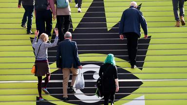 Menschen laufen über eine Treppe mit Logo der Leipziger Buchmesse 2026