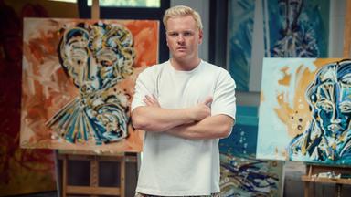 Ein junger Mann in einem Atelier. Im Hintergrund Leinwände auf Staffeleien.