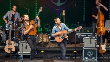 Mehrere Gitarristen und ein Bassist spielen auf einer Bühne.