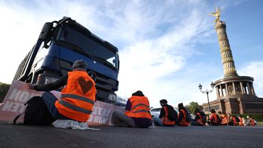 Aktivisten der Letzten Generation sitzen auf der Fahrbahn an der Siegessäule in Berlin und blockieren den Verkehr