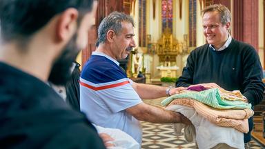 Pfarrer übergibt Decken und Bettwäsche an mehrere Geflüchtete in Kirche.