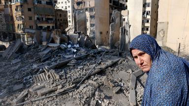 Frau schaut auf Trümmer eines zerstörten Wohnhauses