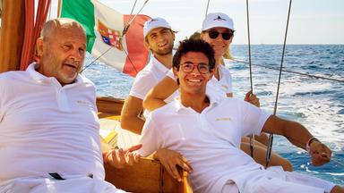 Mehrere Menschen liegen auf einem Segelboot und lächeln glücklich.