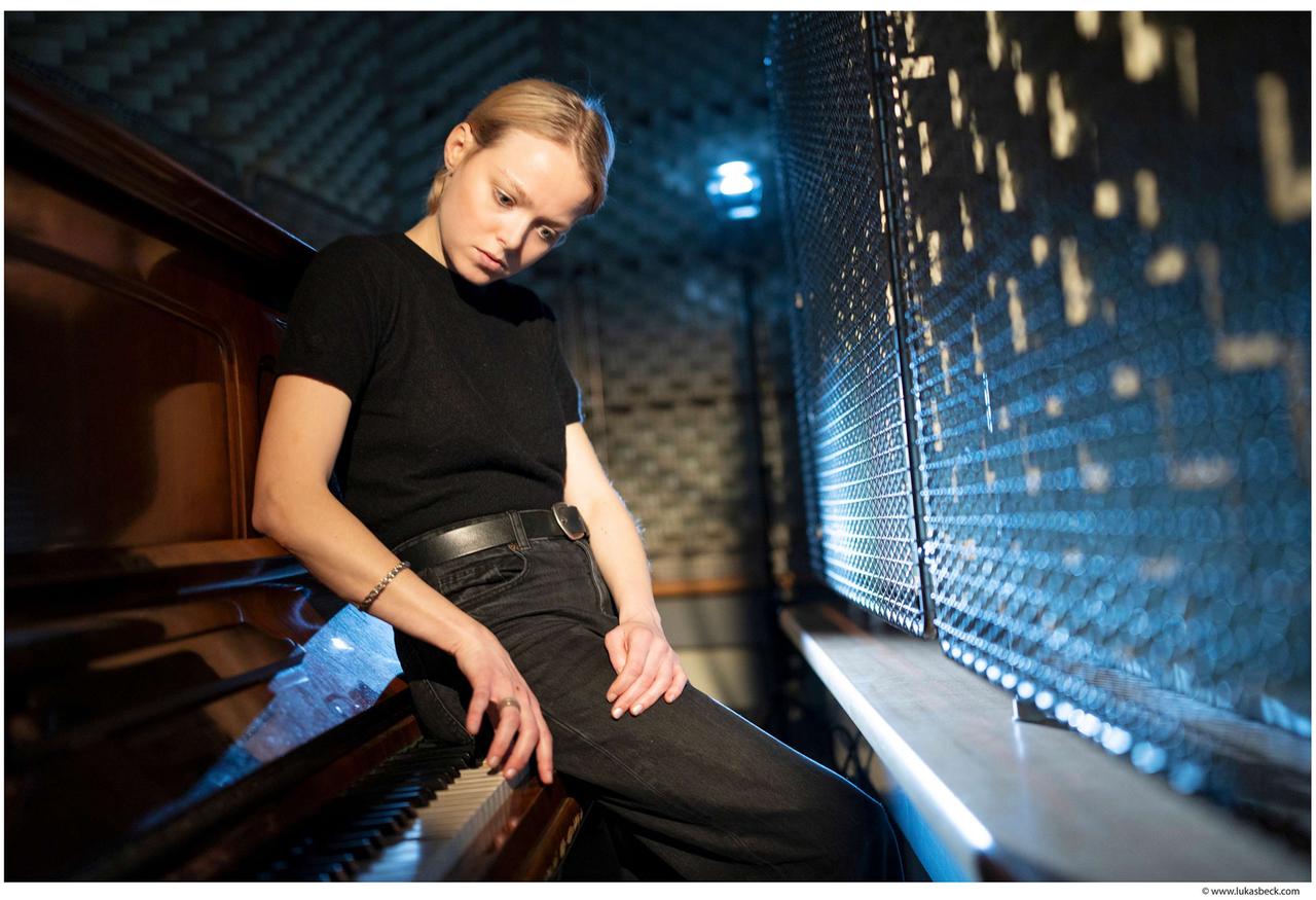 Schauspielerin Marie-Luise Stockinger in einem Tonstudio, an ein Klavier gelehnt.