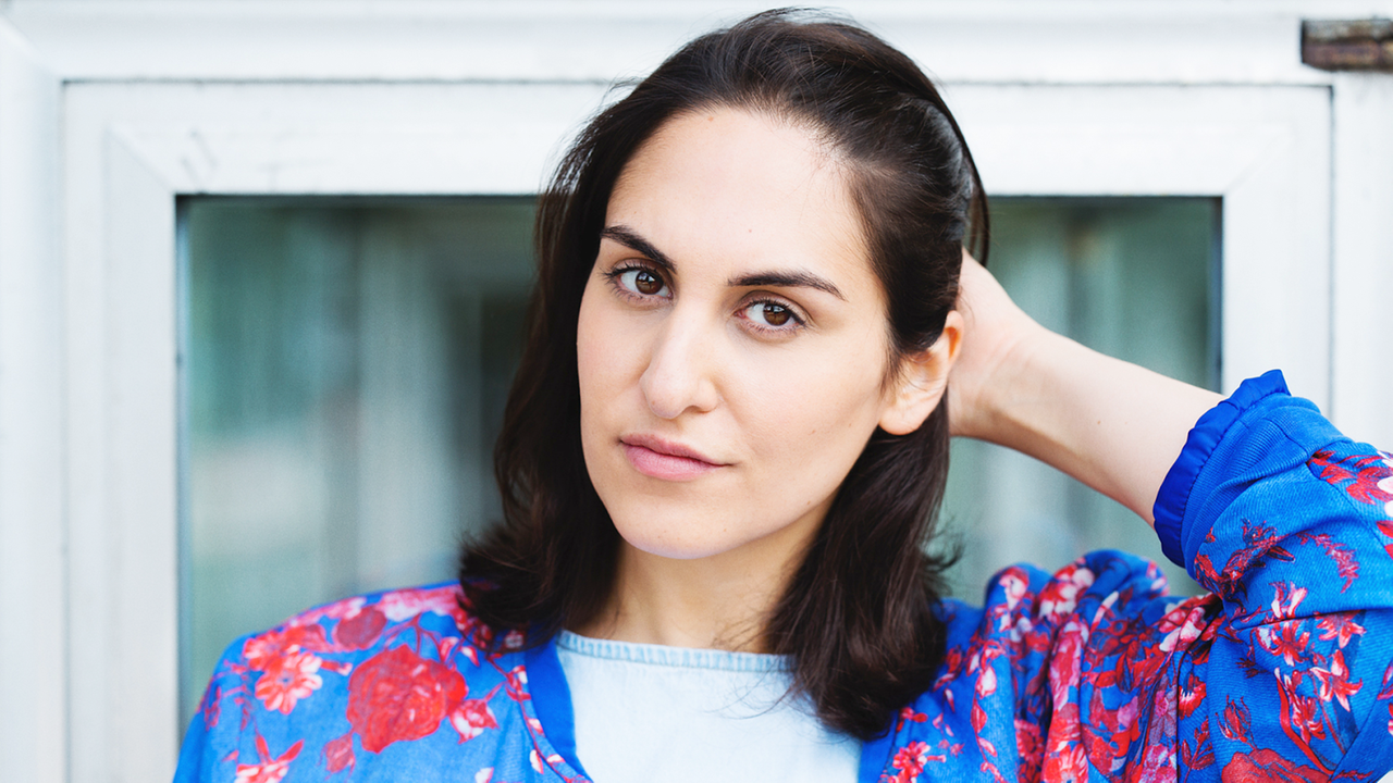 Eine junge Frau mit langen Haaren blickt in die Kamera.