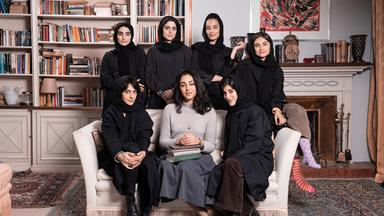 Sieben schwarz gekleidete Frauen, von denen mehrere ein Kopftuch tragen, sitzen in einem Sessel, bzw. stehen dahinter für ein Gruppenfoto.