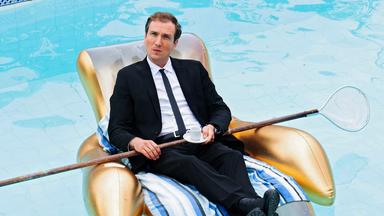 Ein Mann sitzt in einem aufblasbaren Stuhl in einem Pool und hält eine Espressotasse und einen Pool-Kescher in den Händen