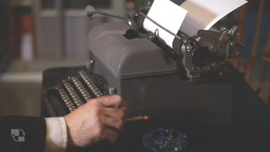 Das Bild zeigt eine Schreibmaschine, die auf einem Tisch platziert ist. Die Schreibmaschine ist in Grau gehalten und hat eine klassische Bauweise. Vor der Schreibmaschine befindet sich ein offenes Blatt Papier, das teilweise über die Walze hinausragt.   In dem Bild ist auch eine Hand zu sehen, die eine Zigarette hält. Die Hand gehört wahrscheinlich zu einer Person, die an der Schreibmaschine sitzt. Die Umgebung ist schwach beleuchtet, was eine nachdenkliche oder nostalgische Atmosphäre schafft. Gegenüber der Schreibmaschine ist ein blauer Aschenbecher sichtbar.   Im Hintergrund sind unscharfe Regale oder andere Möbelstücke zu erkennen, die möglicherweise mit Büchern oder Dokumenten gefüllt sind. Die gesamte Komposition des Bildes vermittelt den Eindruck eines historischen oder journalistischen Settings, das auf vergangene Zeiten hinweist.