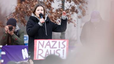 Frau mit Mikrofon, davor Plakat "Nazis raus"