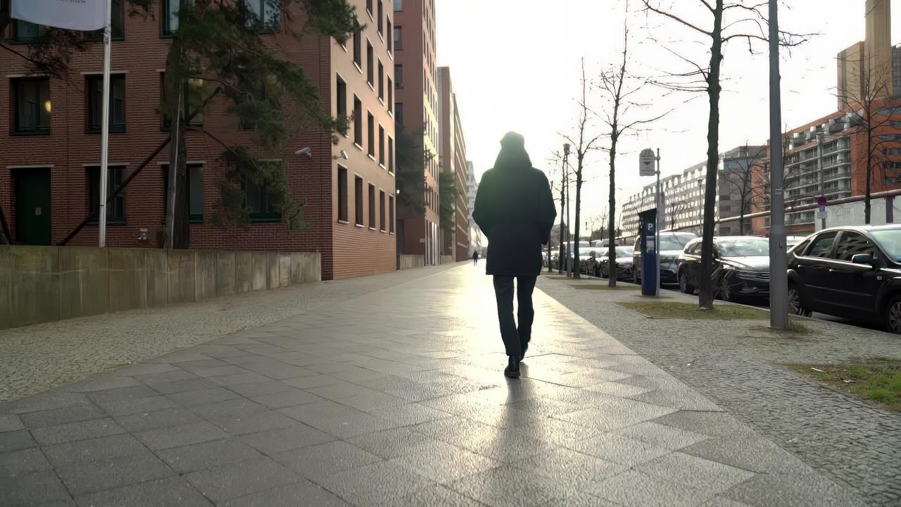 Mann läuft auf Bürgersteig Richtung Horizont/Sonne