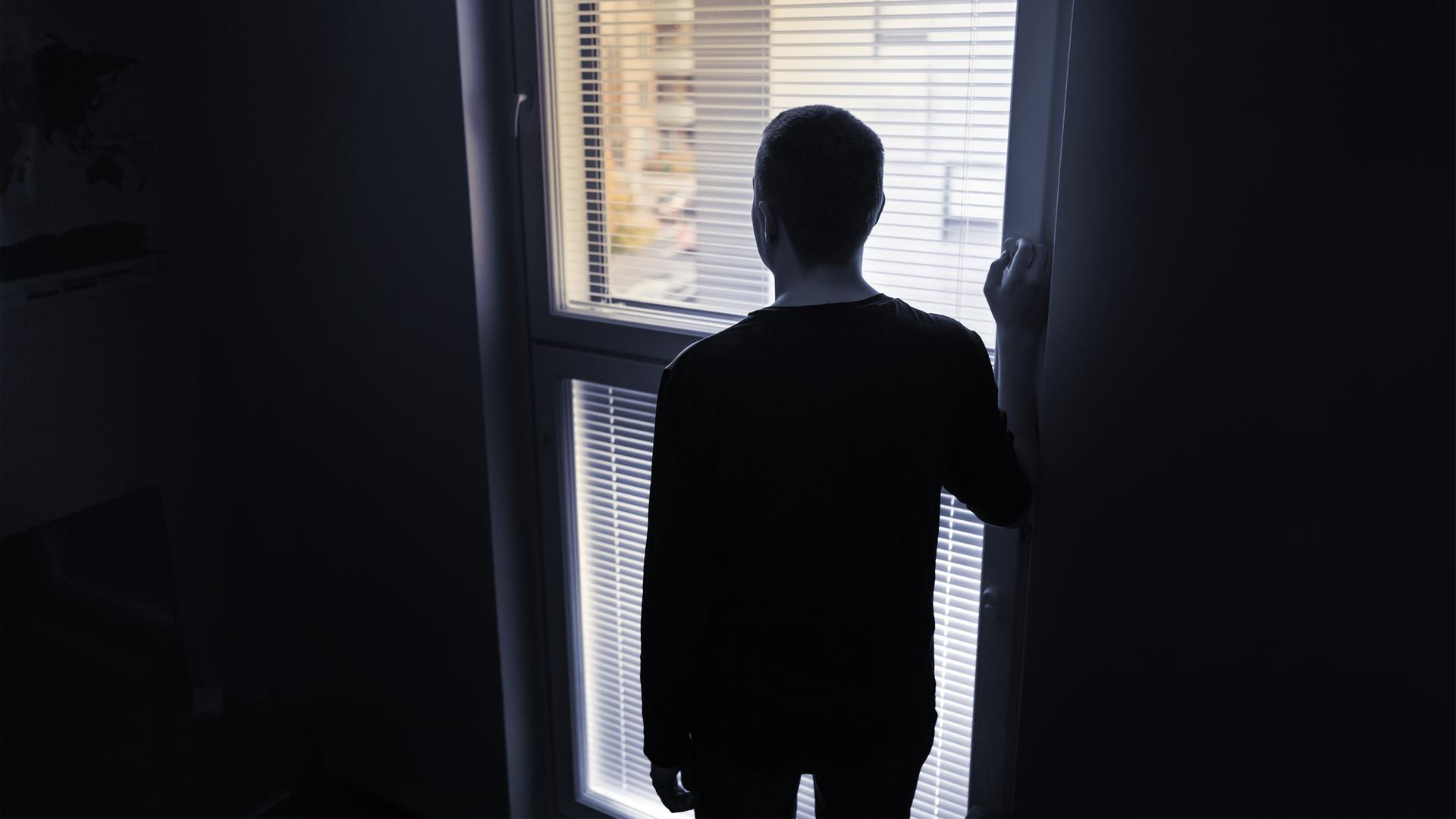die Silhouette eines Mannes von hinten, der vor einem Fenster steht