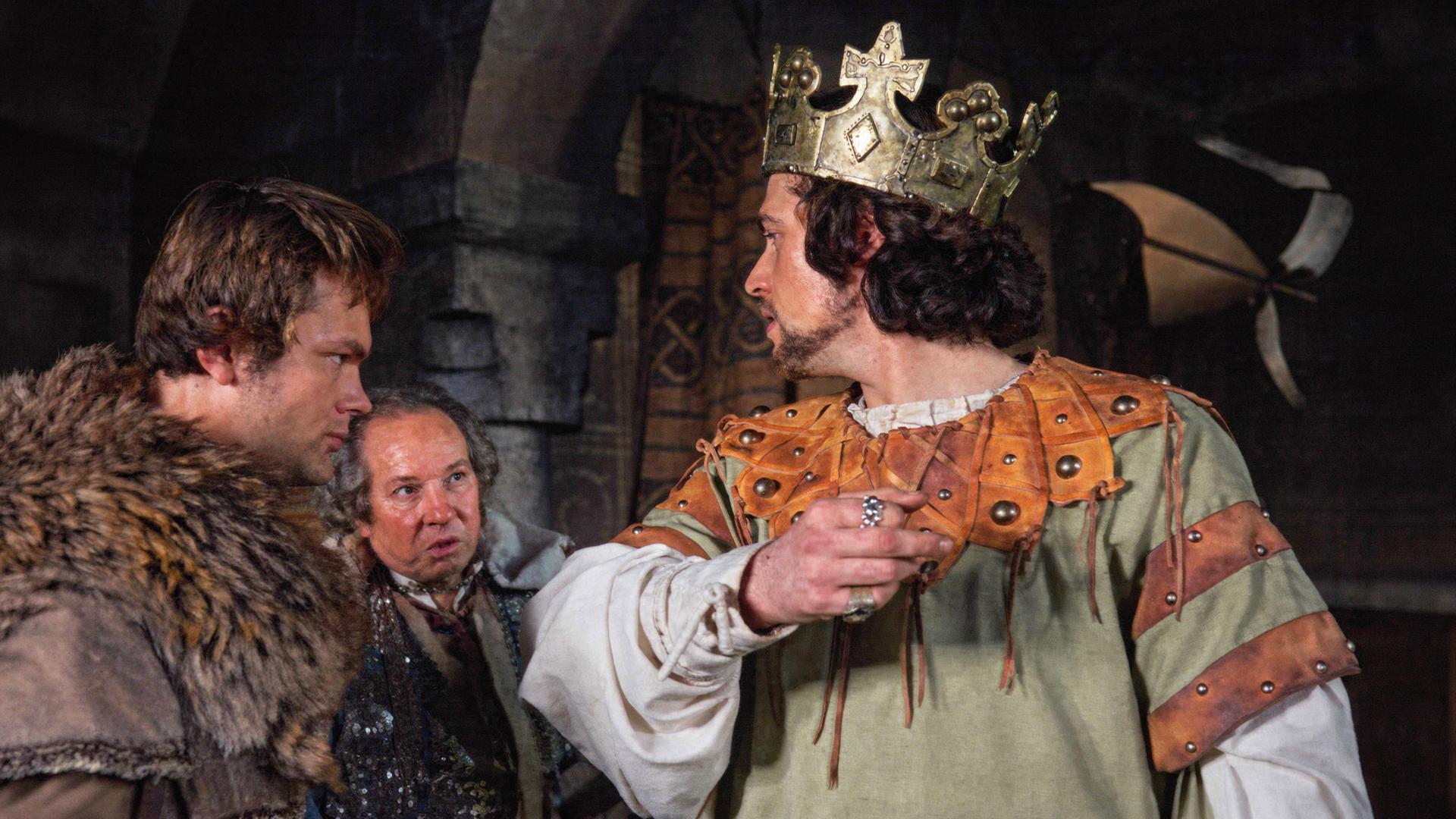 Macbeth (Jon Finch) trägt die Königskrone und wendet sich halb über die Schulter schauend an die beiden Mordgesellen (Michael Balfour, Andrew McCulloch), die neben ihm stehen.