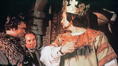 Macbeth (Jon Finch) trägt die Königskrone und wendet sich halb über die Schulter schauend an die beiden Mordgesellen (Michael Balfour, Andrew McCulloch), die neben ihm stehen.