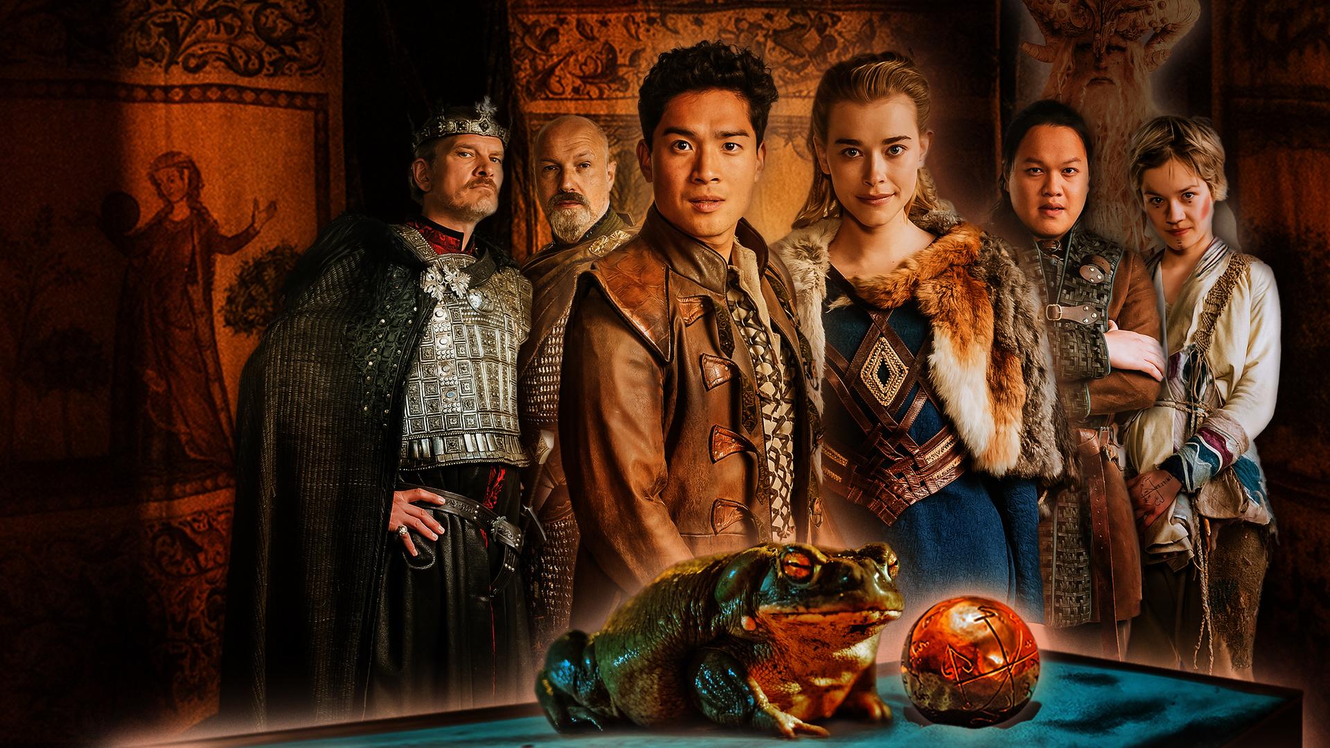 Sechs Personen in mittelalterlichen Gewändern schauen den Betrachter an. Von links: Neben einem groß gewachsenen älteren König, gespielt von Götz Otto, steht ein kräftiger Waffenmeister, gepielt von Simon Werner. Im Vordergrund in der Mitte präsentieren sich ein junger Prinz asiatischer Abstammung, verkörpert von Jan Liem, und eine blonde Prinzessin in einem blauen Kleid, dargestellt von Milena Tscharntke. Wieder etwas im Hintergrund sieht man einen jüngeren Mann mit schwarzen Haaren, gespielt von Anh Alexander Tran, und eine junge Frau mit kurzen blonden Haaren, verkörpert von Lea Drinda. Hinter ihnen sind braune bemalte Tücher gespannt. Ganz im Vordergrund sitzt ein Frosch neben einer goldenen Kugel.