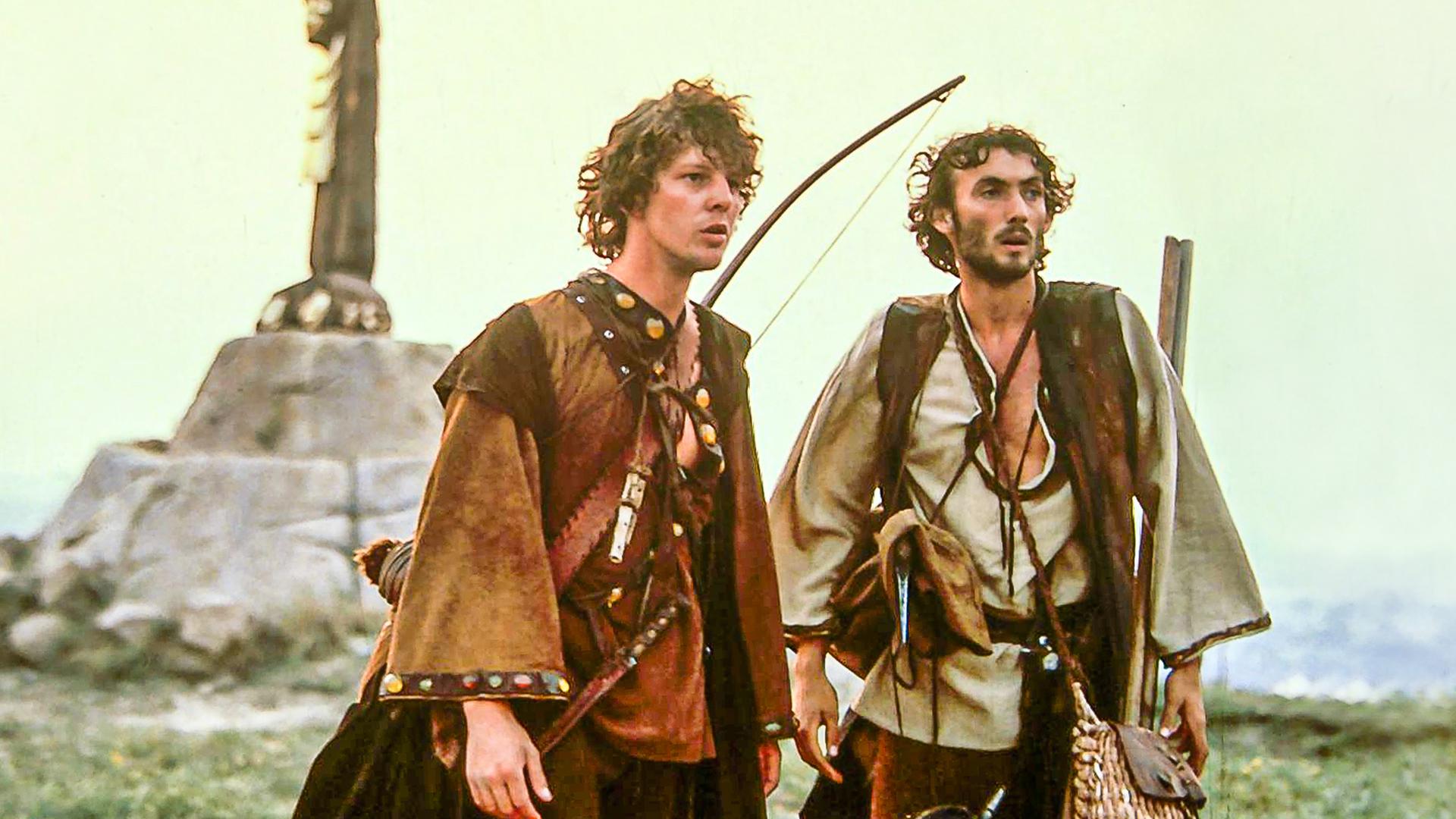 Prinz Martin (Remi Martin) steht zusammen mit seinem Diener Johannes (Valdimir Hajdu) auf einer Wiese und blickt in die Ferne. Der Prinz trägt einen Bogen auf dem Rücken und eine gefüllte Tasche. Beide sind zur Jagd ausgerüstet.