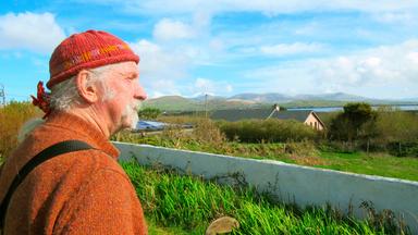 Ein Mann im Profil blickt über die Felder und Häuser aufs Meer.