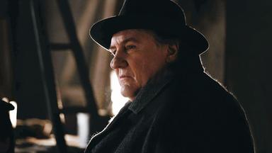 Nahaufnahme: Maigret (Gérard Depardieu) trägt einen dunklen Mantel mit dunklen Hut und blickt nachdenklich und skeptisch zur Seite.