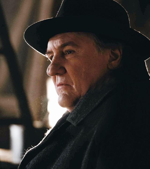 Nahaufnahme: Maigret (Gérard Depardieu) trägt einen dunklen Mantel mit dunklen Hut und blickt nachdenklich und skeptisch zur Seite.