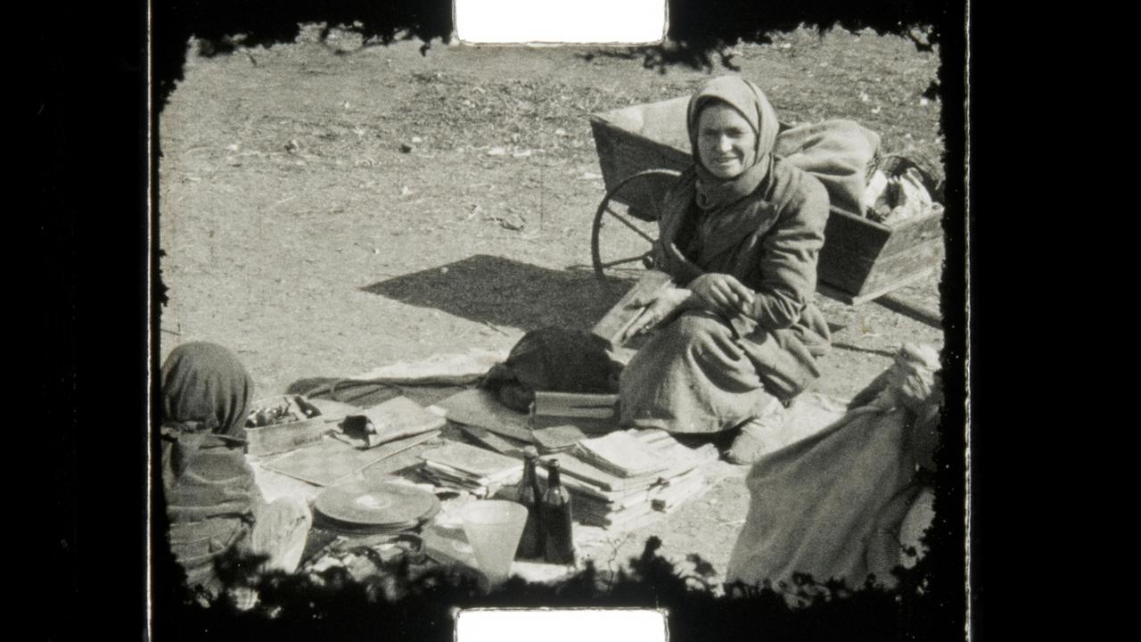 Eine Frau sitzt mit diversen Gegenständen vor einem Karren