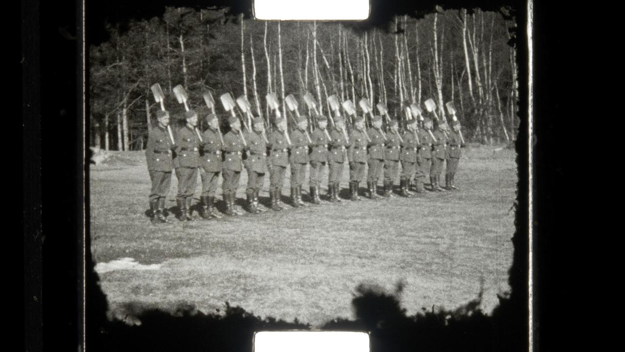 Diverse Soldaten mit einer Schaufel auf ihrer Schulter liegend, nebeneinander stehend auf einer Wiese