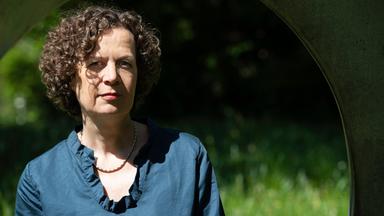 Eine Frau mit kurzem, lockigem Haar und einer blauen Bluse blickt lächelnd in die Kamera.