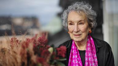 Porträtfoto einer älteren Frau mit grauen Locken, die einen gemusterten pinkfarbenen Schal umgehängt hat.