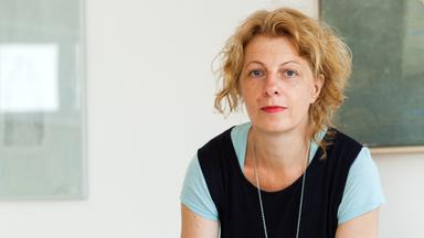 Eine Frau mit roten, lockigen Haaren schaut in die Kamera.