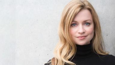 Porträtbild einer jungen Frau mit langen blonden Haaren, die einen schwarzen Rollkragenpullover trägt.