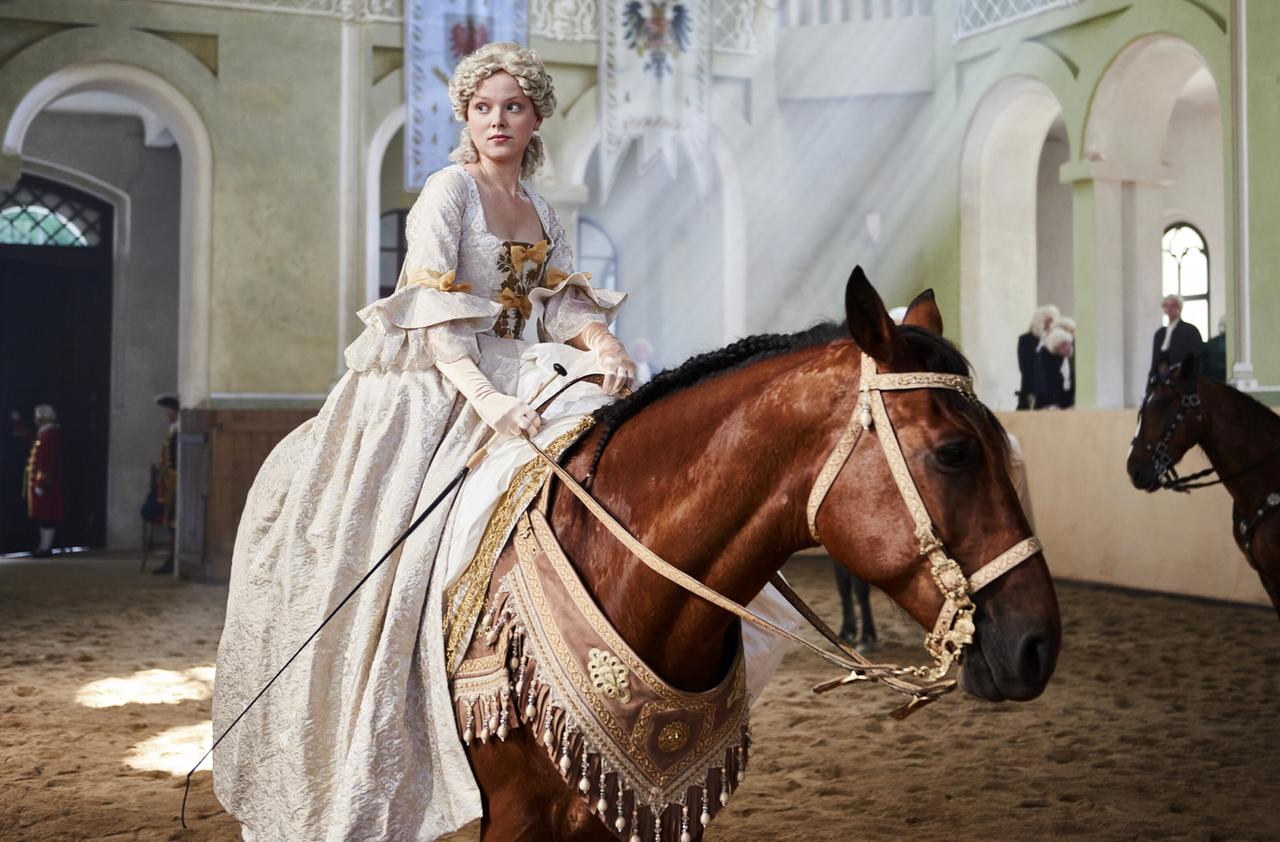 Eine Frau reitet auf einem weissen Pferd in einer historischen Reithalle